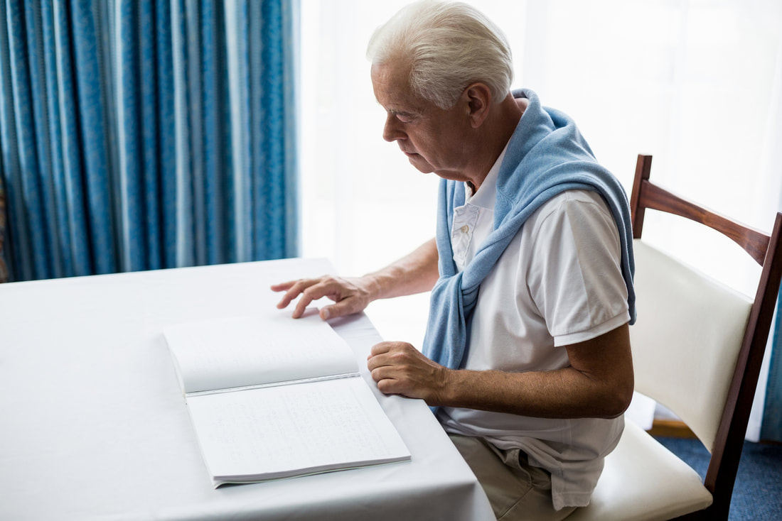 elder man with vision loss is reading a Braille book